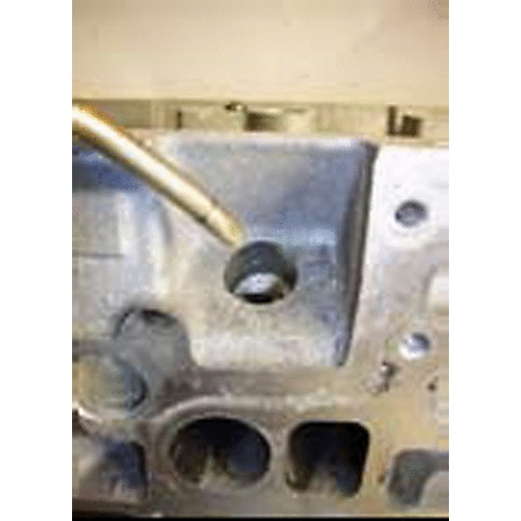 Nahaufnahme eines Zylinderkopfes. Ein Werkzeug berührt eine Bohrung. Im Hintergrund sind weitere Bohrungen und graues Metall zu sehen.